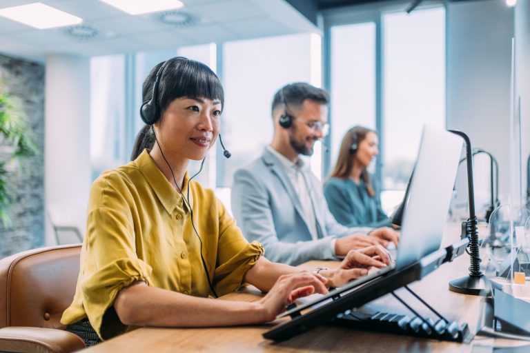 Customer service representatives working together at computers with headsets in a modern office.