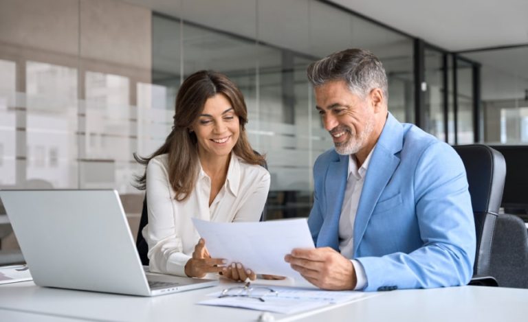 Man and woman collaborating on a document with a laptop in a contemporary office space.